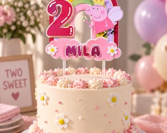 May include: A round cake with light cream frosting, decorated with white daisy flowers and pink sprinkles. A cake topper features a rainbow, a yellow sun, pink clouds, a glittery number 2, and a cartoon pig character with the name MILA.