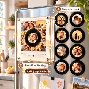 May include: A square acrylic music player frame with a central circular photo slot, mounted on a refrigerator. Eight circular magnetic photo discs are arranged to the right. Text includes '1 Choose a record' and '2 Place it on the player'.