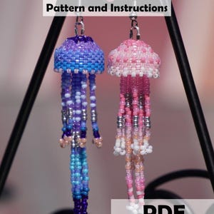 Könnte beinhalten: Seed Bead Jellyfish Earrings Pattern and Instructions PDF Download von StarlightSandStudio. Zwei hängende Quallen-Ohrringe aus kleinen Perlen, einer in Lila- und Blautönen, der andere in Rosa- und Weißtönen, mit langen Tentakeln.