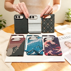 May include: Six rectangular phone cases featuring diverse designs: a black carbon fiber texture, a white textured pattern, a dark grid print, a mountain climber silhouette, a blue mountain landscape, and a stylized wave graphic with a red sun.