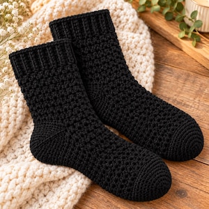 May include: A pair of black crochet socks featuring a textured, repeating stitch pattern throughout the body and a ribbed cuff at the top. The socks are crafted with a dense, uniform black yarn, showcasing a consistent handmade construction.