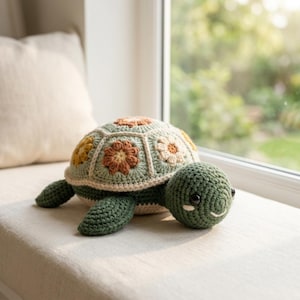 Puede incluir: Un juguete de tortuga tejido a ganchillo con cabeza y aletas de color verde oscuro, con un caparazón formado por parches hexagonales en tonos verde salvia, crema, amarillo mostaza y naranja quemado, cada uno con un diseño floral.