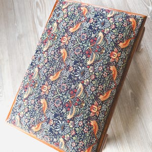 May include: A rectangular footstool with a wooden frame and a padded top upholstered in a dark navy blue fabric featuring a dense, intricate pattern of orange birds, red berries, and green foliage in a repeating botanical design.