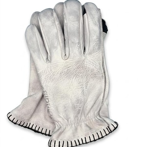 May include: A pair of off-white leather gloves with a distressed texture. The gloves feature black stitching along the cuffs and a subtle embossed logo on the side of the palm area. The design includes a gathered elastic wrist detail for a secure fit.