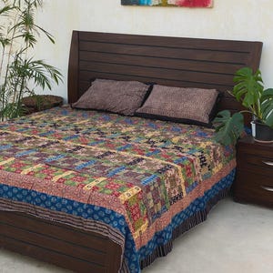 Peut inclure: Un cadre de lit en bois brun foncé avec une tête de lit à lattes horizontales, recouvert d'une courtepointe en patchwork multicolore aux motifs complexes dans des tons de bleu, rouge, vert et jaune, avec deux taies d'oreiller rectangulaires.