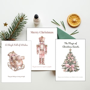 May include: Three white greeting cards featuring watercolor illustrations. One card shows a pink nutcracker with the text Merry Christmas. Another displays a pink sleigh with A Sleigh Full of Wishes. The third depicts a decorated tree with The Magic of Christmas Awaits.