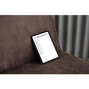 Può includere: Un tablet nero che mostra uno schermo bianco con il testo 02 - ONBOARDING CHECKLIST in carattere nero. Lo schermo elenca varie attività in formato colonna verticale. Il tablet è posizionato contro una superficie marrone testurizzata.