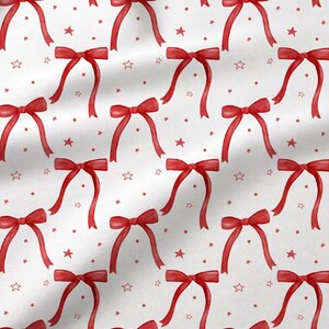 May include: A white fabric featuring a repeating pattern of red bows, small red dots, and red star outlines. The design is arranged in a grid-like layout across the surface, showcasing a consistent festive motif with clean lines and vibrant red.