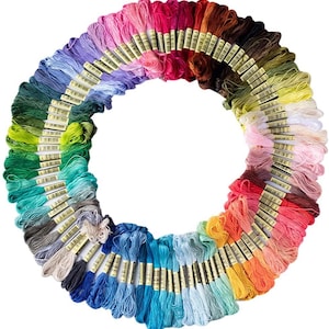 May include: A large circular arrangement of numerous embroidery floss skeins in a wide spectrum of colors, including shades of blue, green, yellow, orange, red, pink, purple, brown, gray, and white, each featuring a small paper label.