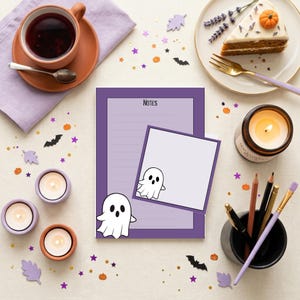 May include: A rectangular notepad with a purple border and the word Notes printed at the top, featuring a white ghost illustration. A smaller square sticky note with a white ghost illustration is placed on top of the notepad.