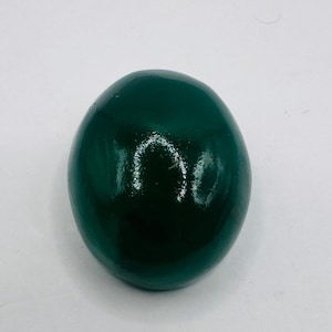 May include: A smooth, rounded, dark forest green object with a glossy, reflective finish. The item has a solid, uniform color and a polished surface that catches the light, creating a bright, circular highlight on its upper curved section.