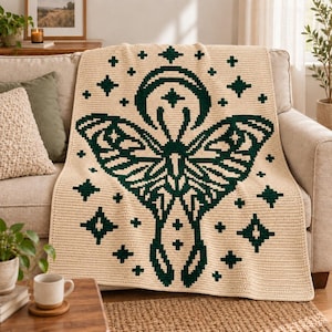 May include: A cream-colored crochet blanket featuring a large, dark green moth graphic centered on the fabric. The moth design is surrounded by various small, dark green star and cross shapes, creating a symmetrical pattern across the textile.