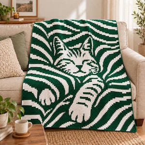 Può includere: Una coperta rettangolare all'uncinetto con uno schema di colori verde scuro e bianco. Il design mostra un muso di gatto stilizzato e zampe integrate in un motivo a strisce ondulate tipo zebra che copre l'intera superficie del tessuto.