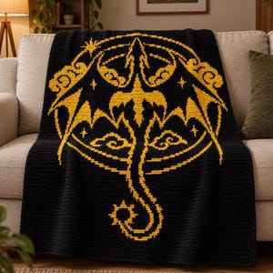 May include: A black crochet blanket featuring a large, centred yellow graphic of a dragon silhouette enclosed within a circular frame. The design includes stylised cloud motifs and small star shapes surrounding the dragon, all rendered in a pixelated style.