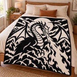 Può includere: Una coperta rettangolare all'uncinetto con un design pixelato in bianco e nero ad alto contrasto. Il motivo raffigura un grande drago con le ali spiegate davanti a una luna circolare, che sputa un getto di fuoco verso il bordo inferiore.