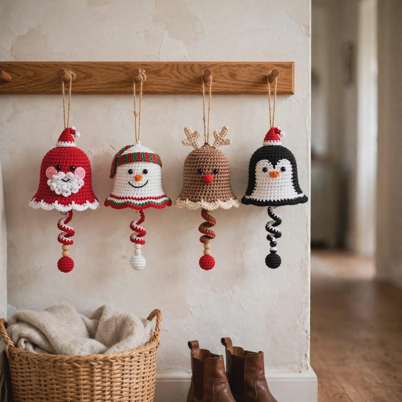 May include: Four crocheted bell ornaments hanging from a wooden rack. The set includes a red Santa, a white snowman with a striped hat, a tan reindeer with antlers, and a black and white penguin. Each bell features a spiral tail and a wooden bead.