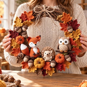 May include: A round grapevine wreath decorated with crocheted autumn leaves in shades of red, orange, and yellow. The wreath features crocheted figures of a fox, a hedgehog, and an owl, along with small crocheted pumpkins and acorns attached throughout.