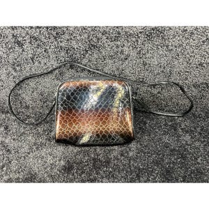 May include: A small crossbody bag featuring a glossy, textured finish with a snakeskin-like pattern. The bag displays a gradient color scheme transitioning from dark black at the top to a warm brown and tan hue toward the bottom, with a thin strap.