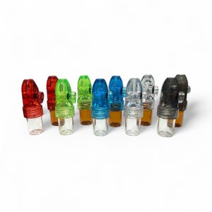 May include: A collection of ten small, cylindrical snuff bullets arranged in a row. Each unit features a clear glass base and a coloured plastic top with a side-mounted dispensing nozzle. The colours include red, green, blue, clear, and black.