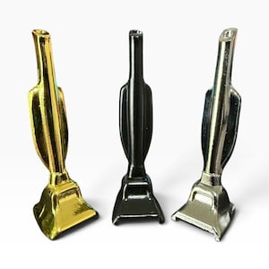 May include: Three upright vacuum cleaner attachments arranged in a row. The left attachment has a shiny gold finish, the centre attachment has a matte black finish, and the right attachment has a polished silver metallic finish. Each piece is identical.