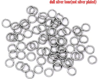 May include: A large pile of silver-toned jump rings. The rings are small and round, and they are all the same size. The rings are made of metal and have a dull finish. The text "dull silver tone (not silver plated)" is written in red above the rings.
