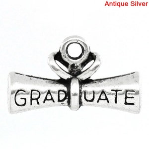 May include: Antique silver charm in the shape of a graduation scroll with the word "GRADUATE" inscribed on it. The charm has a loop at the top for attaching to a necklace or bracelet.