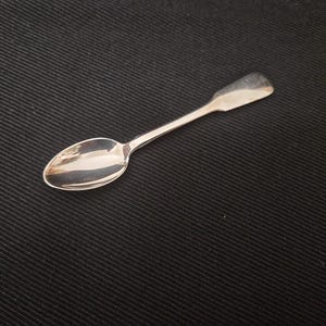 Peut inclure: Une cuillère en métal argenté poli dotée d'un cuilleron ovale lisse et d'un manche plat et effilé. La cuillère présente une surface réfléchissante et brillante qui capte la lumière, révélant un design simple et épuré sans motifs ni gravures.