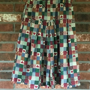 May include: A knee-length skirt with a patchwork design, featuring squares of various patterns and colors, including red hearts. The skirt is hanging on a clothesline against a brick wall.