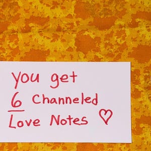 Könnte beinhalten: Eine weiße rechteckige Karte mit dem roten handschriftlichen Text you get 6 Channeled Love Notes und einem Herzsymbol. Zwei kleine Glasfläschchen mit Korkstopfen und eine weiße Muschel mit drei blauen und grauen Steinen liegen daneben.