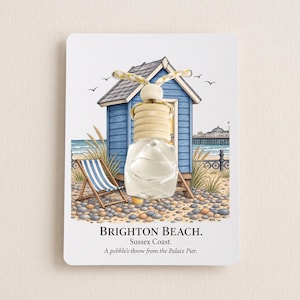 May include: A small glass car air freshener bottle with a wooden cap and hanging cord, mounted on a card featuring an illustration of a blue beach hut, a striped deck chair, and the text BRIGHTON BEACH. Sussex Coast. A pebble's throw from the Palace Pier.