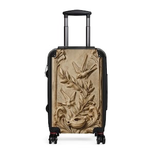 May include: A black rolling suitcase featuring a front panel with a beige, stone-like relief print. The design displays two flying birds, leafy branches, and an oil lamp, all rendered in a carved, sculptural style with intricate scrollwork details.