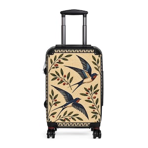 May include: A black rolling suitcase featuring a beige front panel decorated with two flying swallows and olive branches with red berries. The top and bottom edges are bordered by a black and gold Greek key pattern design.