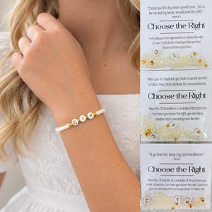 May include: A white beaded bracelet featuring three central white beads with the gold letters C, T, and R, accented by small gold spacer beads. The bracelet is displayed alongside three white cards with religious text and the phrase Choose the Right.