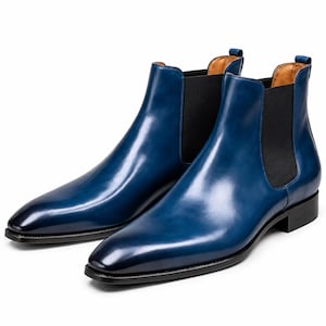 Könnte beinhalten: Ein Paar polierte Chelsea-Stiefel aus blauem Leder mit glatter Oberfläche, schwarzen elastischen Seiteneinsätzen, spitzer Zehenpartie und niedrigem schwarzem Absatz. Jeder Stiefel hat eine kleine Zuglasche am hinteren Schaft und ein beiges Innenfutter.
