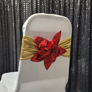 May include: White chair cover with a gold sash and a red poinsettia flower decoration.