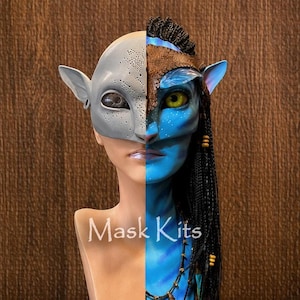 Puede incluir: Una m&aacute;scara de cara dividida sobre una cabeza de maniqu&iacute;. El lado izquierdo es una m&aacute;scara gris claro lisa de tipo alien&iacute;gena con peque&ntilde;as perforaciones. El lado derecho es una m&aacute;scara azul inspirada en los Na'vi con un ojo amarillo y trenzas.