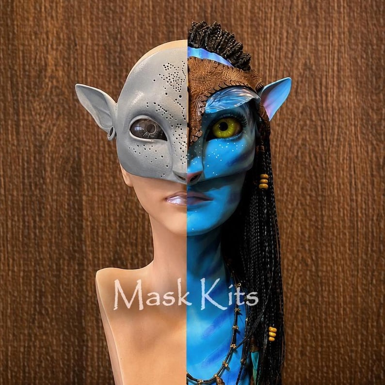 Puede incluir: Una m&aacute;scara de cara dividida sobre una cabeza de maniqu&iacute;. El lado izquierdo es una m&aacute;scara gris claro lisa de tipo alien&iacute;gena con peque&ntilde;as perforaciones. El lado derecho es una m&aacute;scara azul inspirada en los Na'vi con un ojo amarillo y trenzas.