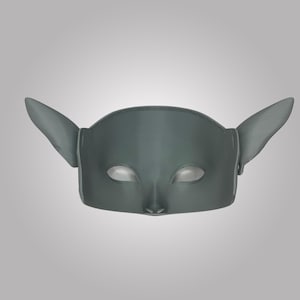 Puede incluir: Una m&aacute;scara gris s&oacute;lida con una superficie lisa y contorneada, dos aberturas para los ojos en forma de almendra, un puente nasal puntiagudo y dos orejas grandes y puntiagudas que se extienden hacia los lados. Aspecto moldeado.