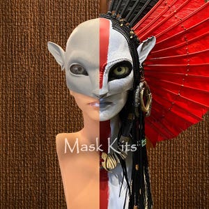 Pode incluir: Uma máscara facial dividida com um design branco e cinza, com uma faixa vermelha e olhos grandes e detalhados. A máscara tem orelhas pontudas e é adornada com tranças pretas, detalhes dourados e um grande leque vermelho. O texto "Mask Kits" é visível.