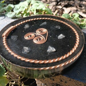 May include: A circular black resin coaster featuring a central copper wire spiral design. The surface is embedded with small, clear, jagged stone fragments and is bordered by a twisted copper wire rim that encircles the entire perimeter.