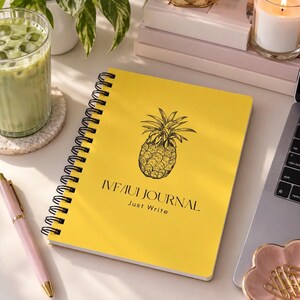 May include: A bright yellow spiral-bound journal featuring a black line-art illustration of a pineapple centered on the cover. The text "IVF/IUI JOURNAL" and "Just Write" are printed in black below the pineapple graphic on the front cover.