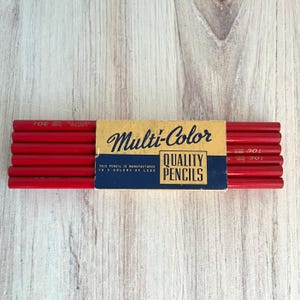 May include: A set of red pencils held together by a yellow and blue paper band. The band features the text Multi-Color QUALITY PENCILS and states this pencil is manufactured in 5 colors of lead. The pencils are marked with the text Linton 301.
