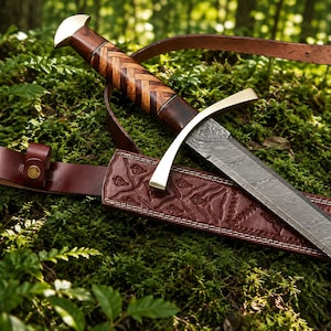 Puede incluir: Una espada con hoja de acero de Damasco estampada, guarda de latón y empuñadura de madera con diseño trenzado. La espada se acompaña de una vaina de cuero rojo oscuro con detalles en relieve y una correa de cuero a juego.