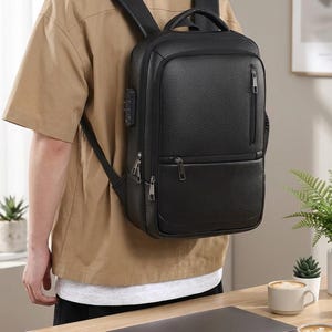 Könnte beinhalten: Ein schwarzer Rucksack mit strukturierter Oberfläche und rechteckiger Form, ausgestattet mit einer vertikalen Reißverschlusstasche vorne, einem horizontalen Reißverschlussfach, einem Tragegriff, gepolsterten Schultergurten und einem seitlichen Zahlenschloss.