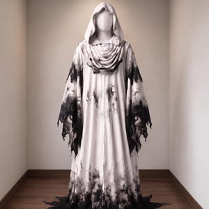 May include: A floor-length hooded robe featuring a white base with a black gradient pattern. The garment includes a draped cowl neckline, long sleeves with jagged, distressed edges, and a hemline that flares out into pointed, uneven sections.