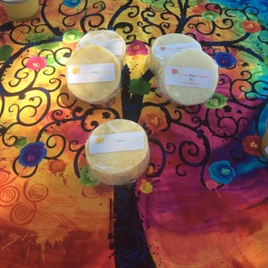May include: Five round bars of soap wrapped in plastic on a colorful patterned fabric. The soap bars are labeled "Aloe" and "Citrus Mint Summer Breeze".