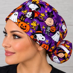 May include: A purple scrub cap featuring a Halloween-themed pattern with Snoopy, Woodstock, and Charlie Brown characters. The fabric displays orange pumpkins, white ghosts, black witch hats, and dark silhouettes of trees against a purple background.