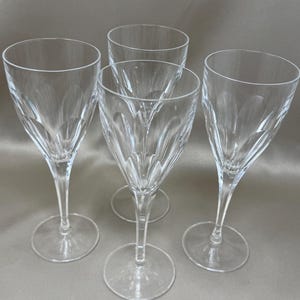 Op de afbeelding: Een set van vier heldere wijnglazen met een verticaal gegroefd patroon rond het onderste gedeelte van de kelk. Elk glas heeft een slanke steel en een ronde voet, wat zorgt voor een transparant ontwerp met reflecterende lichtaccenten.