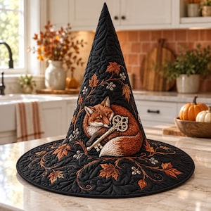 May include: A black quilted witch hat featuring an embroidered orange fox curled up while holding a silver skeleton key. The hat is decorated with detailed stitching of autumn maple leaves and small silver berries across the fabric surface.