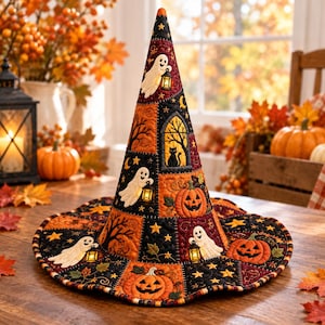 May include: A quilted witch hat featuring a patchwork design in black, orange, and deep red. The fabric displays embroidered motifs of white ghosts holding lanterns, orange jack-o'-lanterns, black cats in windows, and yellow stars.